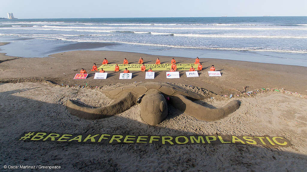 Activistas de Greenpeace México crean una gran escultura de arena de tortuga marina para resaltar el problema de la contaminación plástica, mientras sostienen una manta que dice "Sus envases no desaparecen. Aquí están".