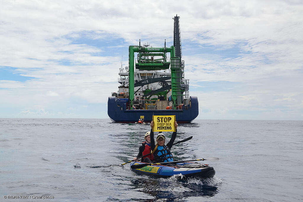 Activistas de Greenpeace en kayaks protestan pacíficamente frente al buque MV COCO en el Océano Pacífico; sostienen mantas que dicen “Stop Deep Sea Mining”.