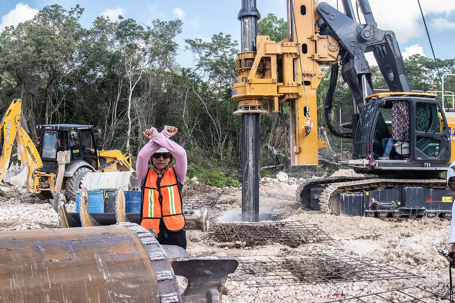 Maquinaria de construcción del Tren Maya operando en la selva, mientras una persona frente a la máquina levanta las manos en señal de protesta, pidiendo que se detenga la destrucción del entorno natural.