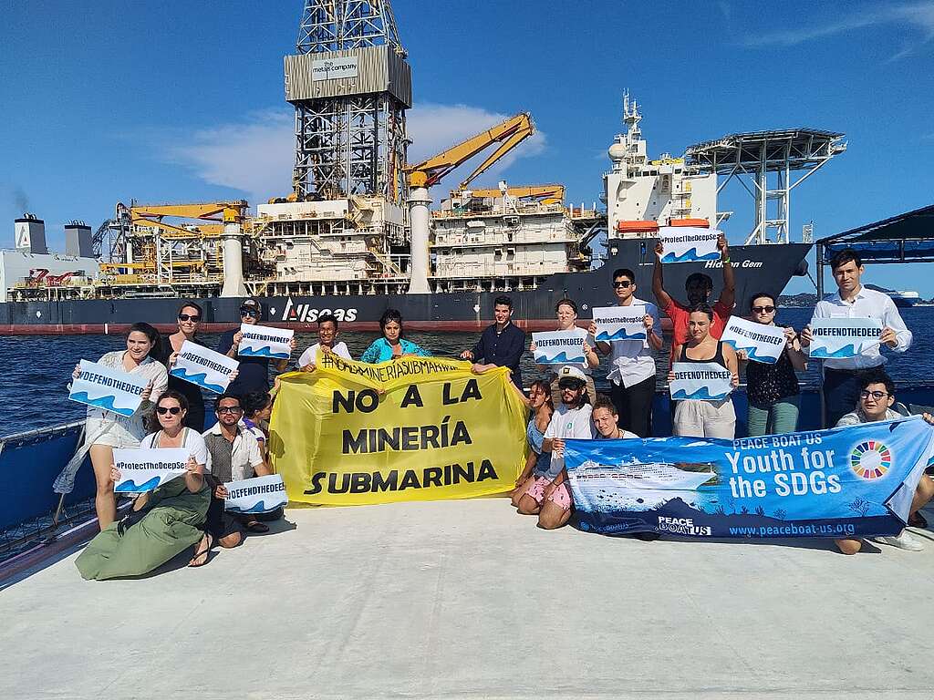 Jóvenes activistas sostienen una manta que dice "No a la minería submarina" y otras más pequeñas con mensajes como "Defiende las profundidades", "Protege el océano profundo" y "Juventud por los ODS".