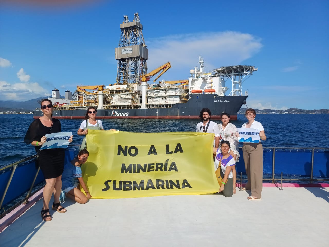 Personas de diversas organizaciones protestan frente al Hidden Gem sosteniendo una manta que dice "No a la minería submarina".