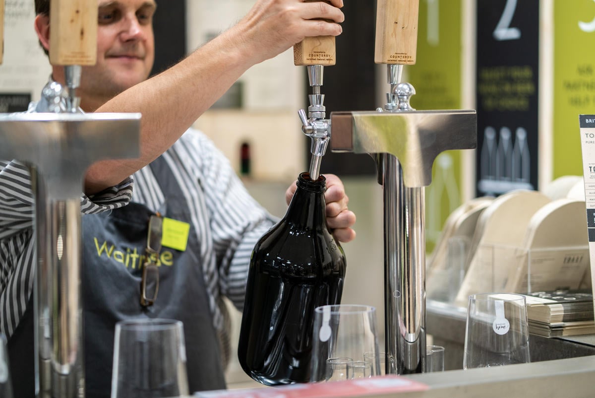 Empleado de un supermercado rellenando una botella de cerveza.