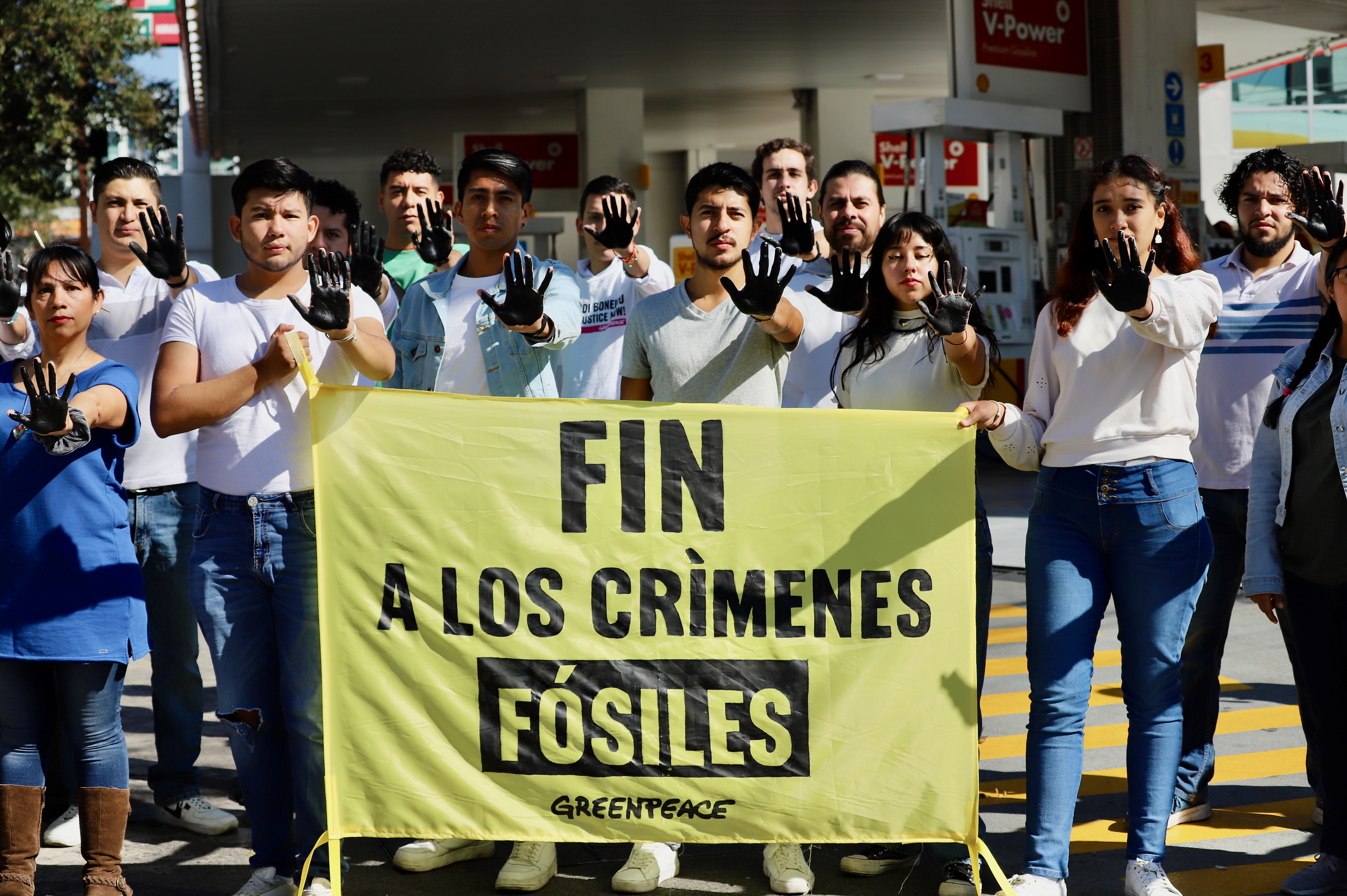 Fotografía de integrantes del voluntariado de Greenpeace México, que sostienen una manta que dice "Fin a los crímenes fósiles" y sus manos están pintadas de negro representando los combustibles fósiles.