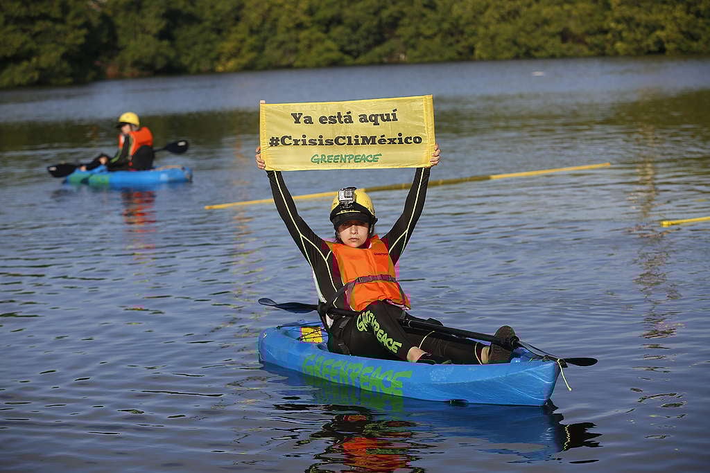 Activista de Greenpeace México en una lancha, sostiene un cartel que dice "Ya está aquí: #CrisisCliMéxico".