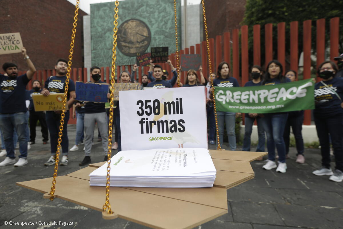 Activista de Greenpeace México protestando con pancartas detrás de una representación simbólica de las 350 mil firmas recabadas para exigir que no haya retrocesos en las reformas a la Ley de Residuos y la Ley de Economía Circular.