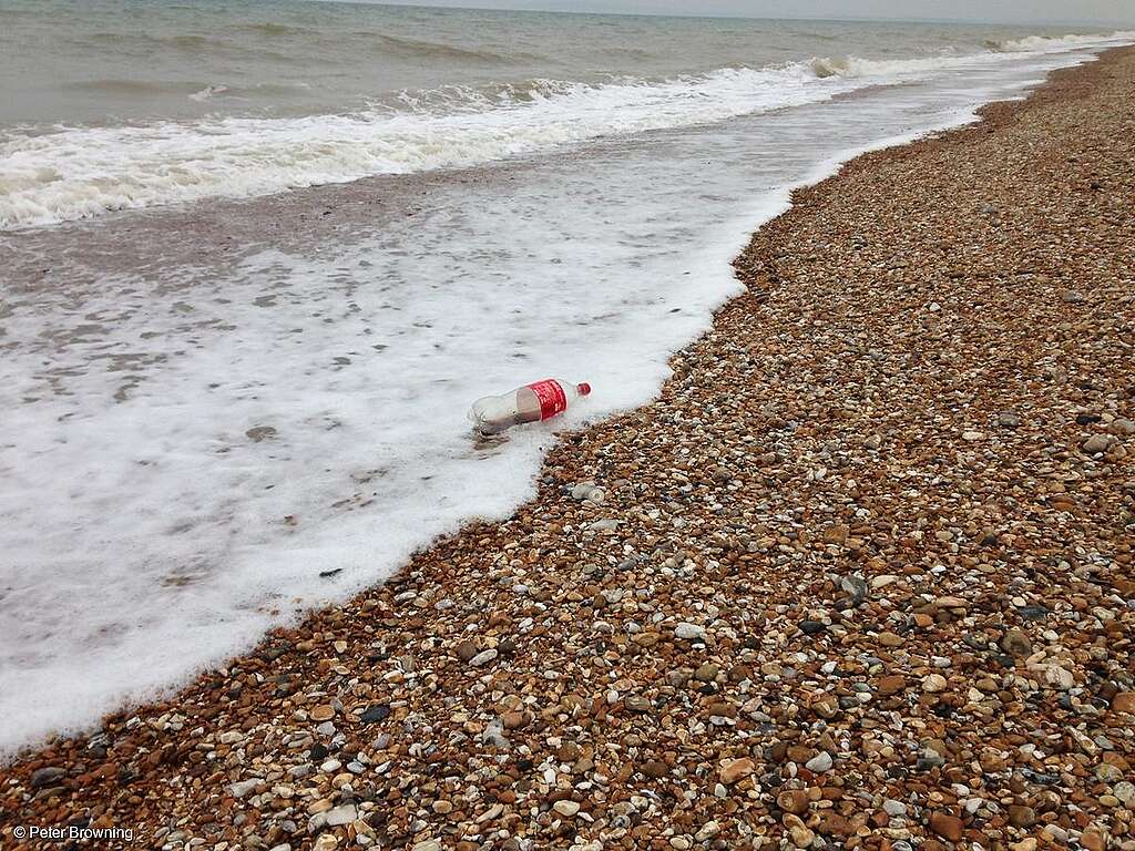 Botella de plástico de Coca-Cola en la playa cerca de Dungeness, Kent, Reino Unido.