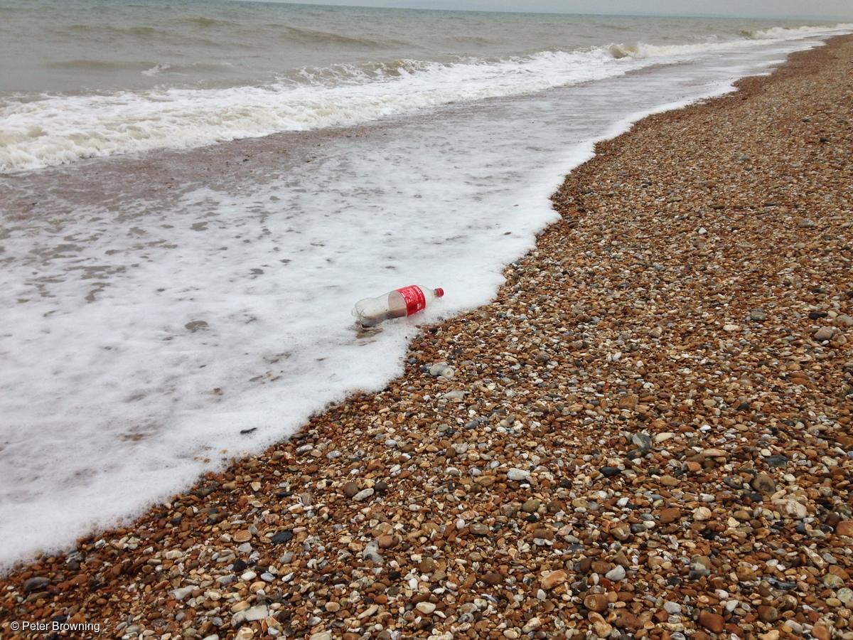 Botella de plástico de Coca-Cola en la playa cerca de Dungeness, Kent, Reino Unido.