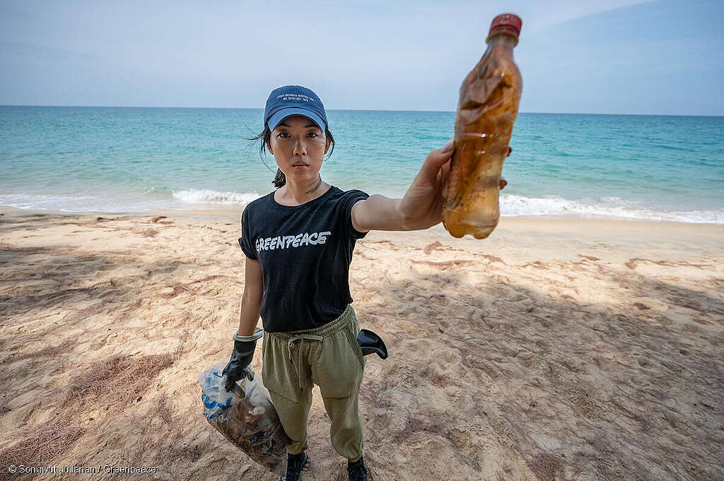 Activista de Greenpeace en la playa sostiene una botella de plástico durante auditoría de marcas.