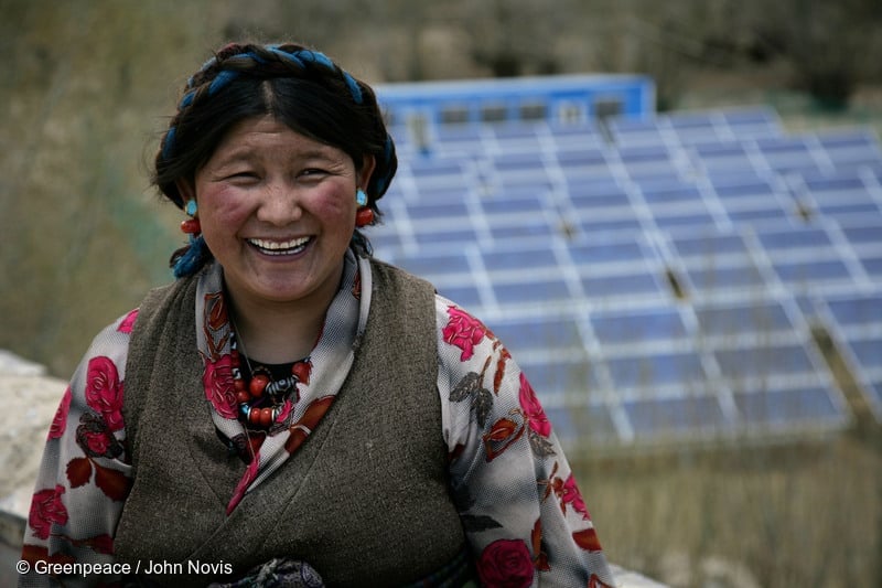 Una mujer tibetana, en la foto aparece con paneles solares al fondo, que suministran energía a su negocio.