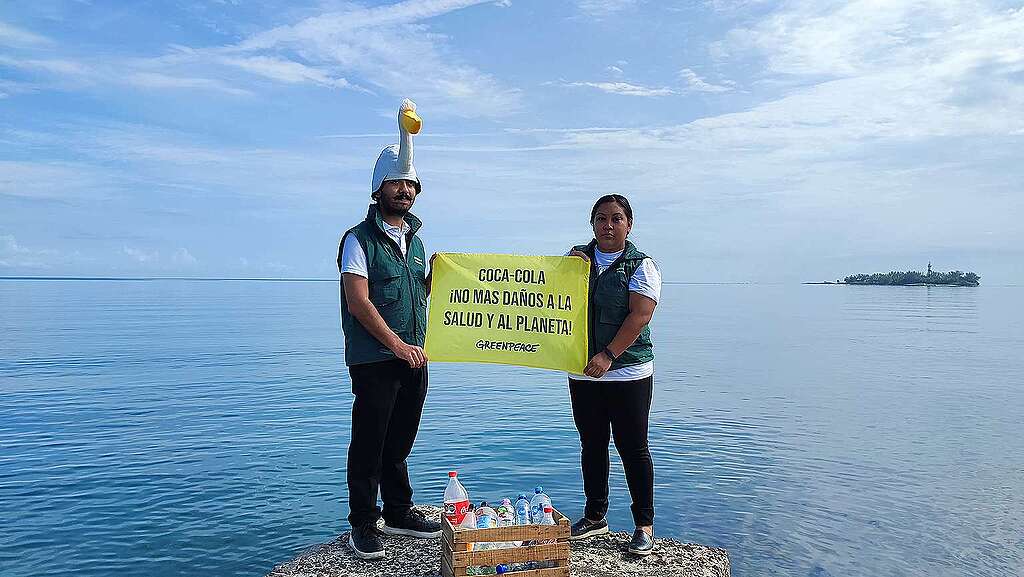 Fotografía panorámica de dos activistas de Greenpeace México en  una laguna sosteniendo una manta que dice "Coca-Cola no más daños a la salud y al planeta".