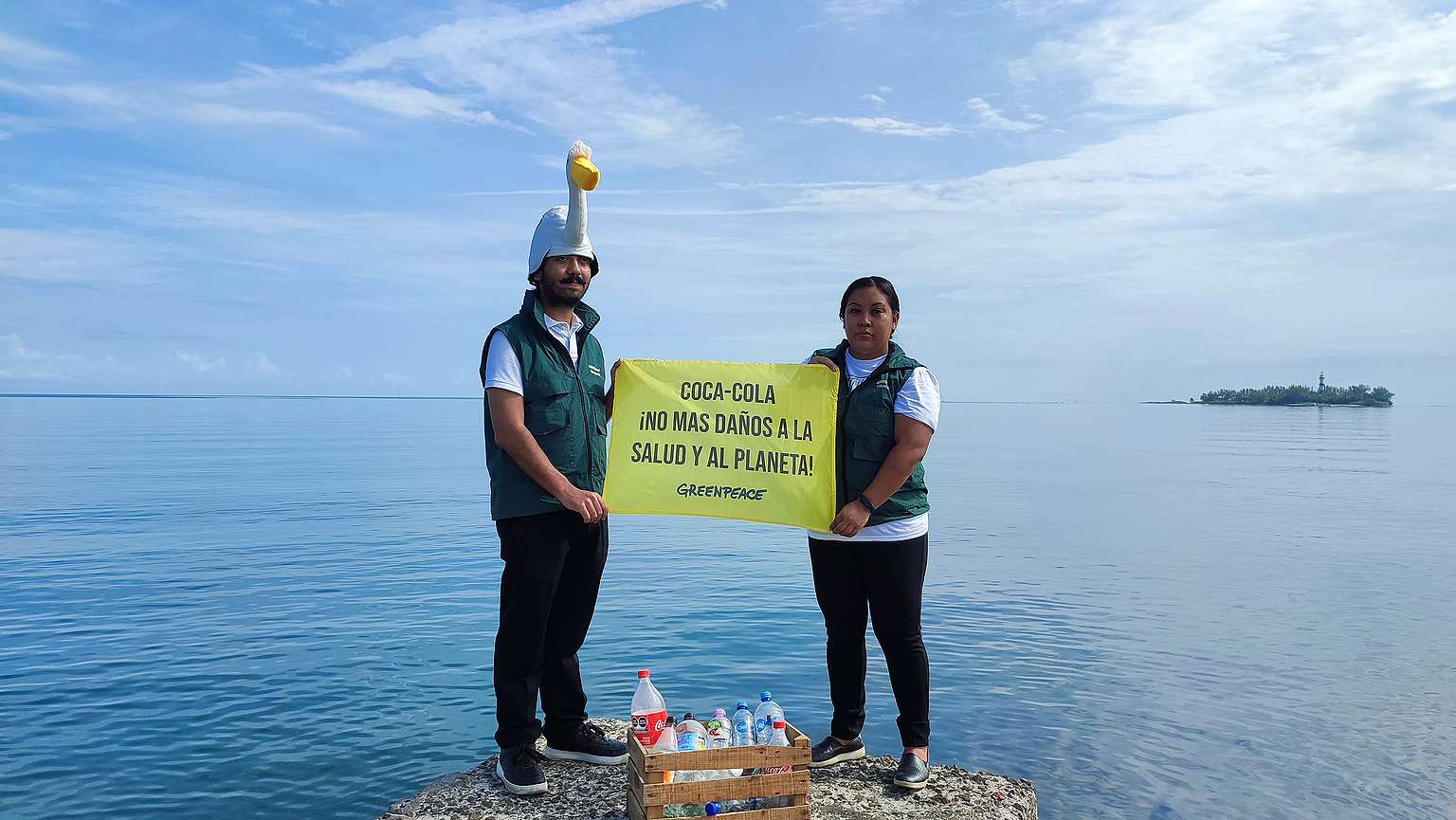 Fotografía panorámica de dos activistas de Greenpeace México en una laguna sosteniendo una manta que dice "Coca-Cola no más daños a la salud y al planeta".