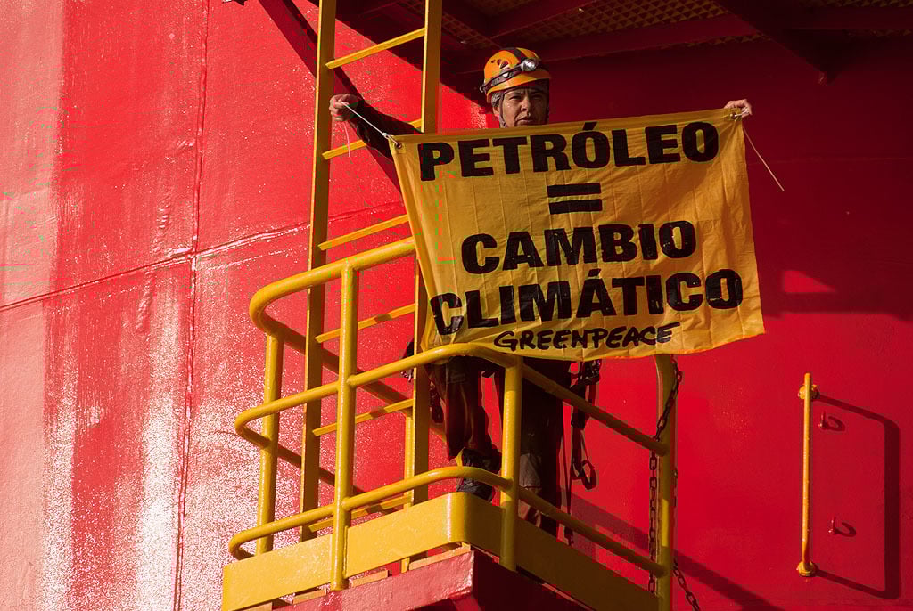 Activista de Greenpeace México sobre una plataforma petrolera sostiene un cartel en que se lee "Petróleo = Cambio climático".