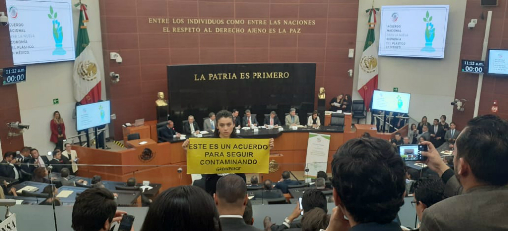 Activista de Greenpeace en el Senado, sostiene una manta en la que se lee "Este es un acuerdo para seguir contaminando".