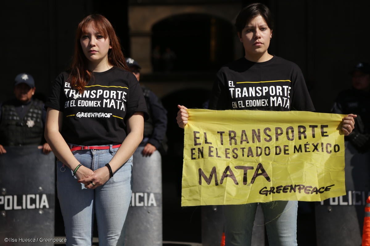 Fotografía de 2 activistas de Greenpeace México, una de ellas sotiene una pancarta que dice "El transporte en el Estado de México mata".