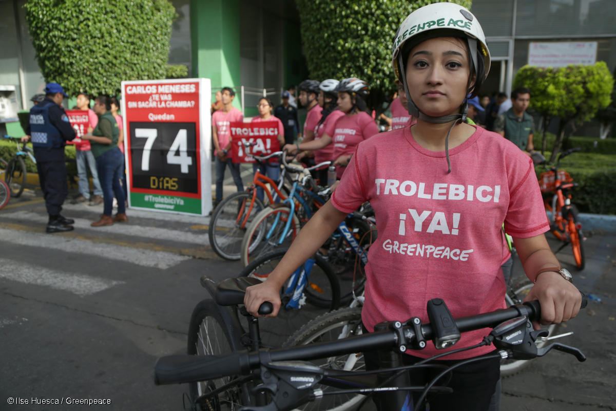 Activista de Greenpeace México junto a su bicicleta, portando una playera en la que se lee "Trolebici YA".