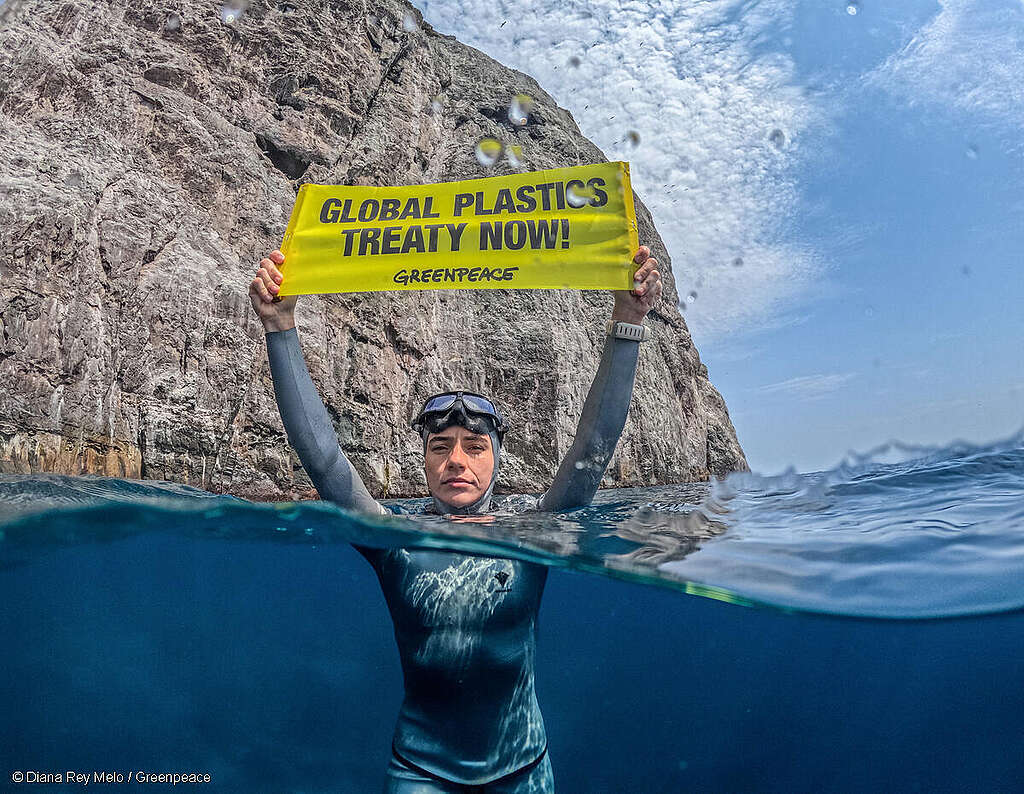 La influencer y apneísta colombiana Sofía Gómez en el mar mientras sostiene un cartel exigiendo un Tratado Global de Plásticos.