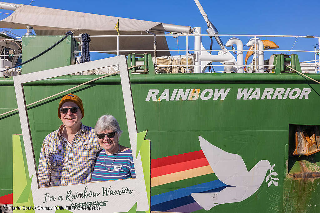 Fotografía de simpatizantes de Greenpeace junto al Rainbow Warrior, portan un marco fotográfico con la leyenda "Yo soy un Guerrero del Arcoíris".