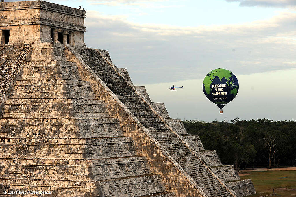 Toma aérea de la zona arqueológica de Chichén Itzá en la que se observa un globo aerostático de fondo con la leyenda "Protejan el clima" en el marco de la COP16.