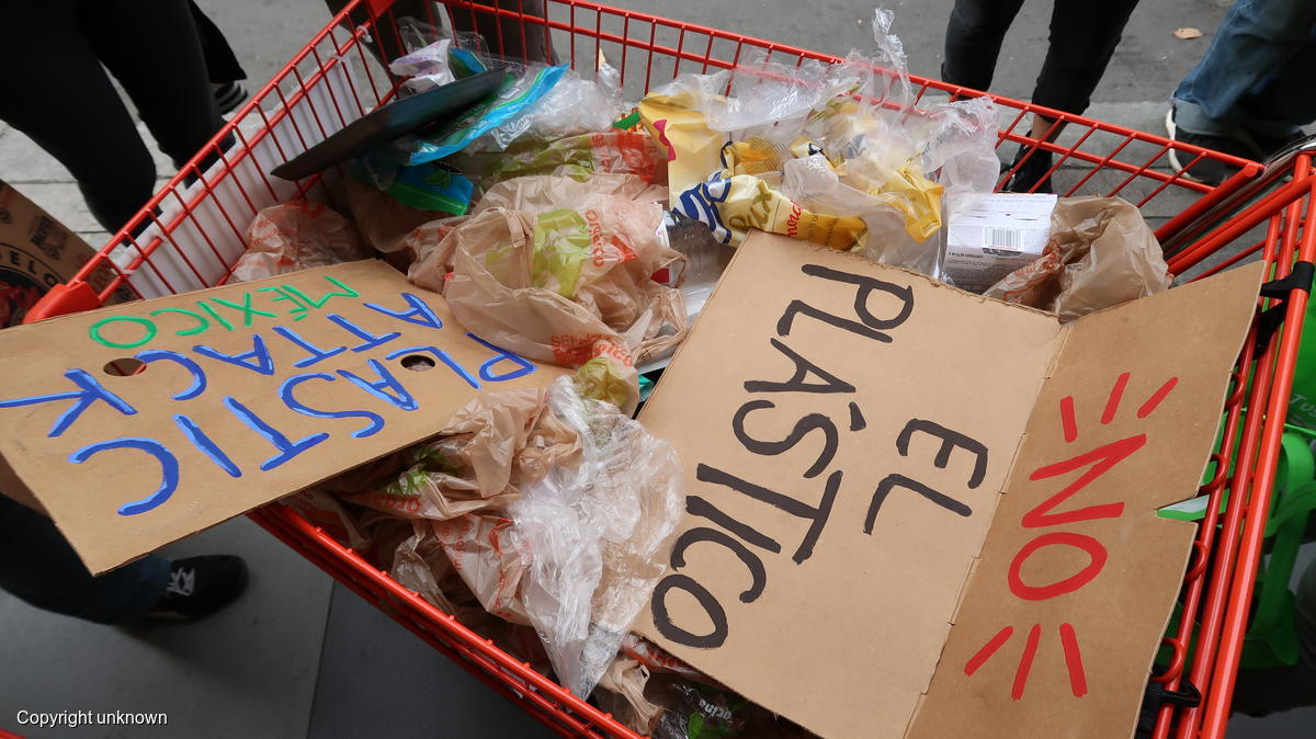 Fotografía de un carrito de supermercado lleno de residuos plásticos y con los mensajes "No al plástico" y "El plástico ataca México".