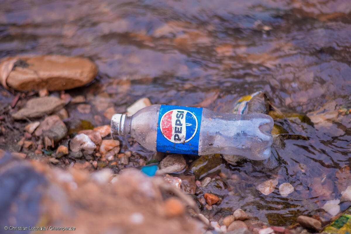 Fotografía de una botella de refresco de la marca Pepsi, tirada en un riachuelo.