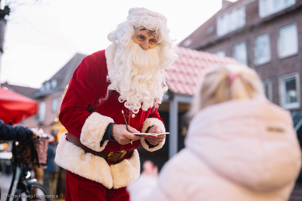 Fotografía de un voluntario de Greenpeace disfrazado de Papá Noel mientras habla con una niña.