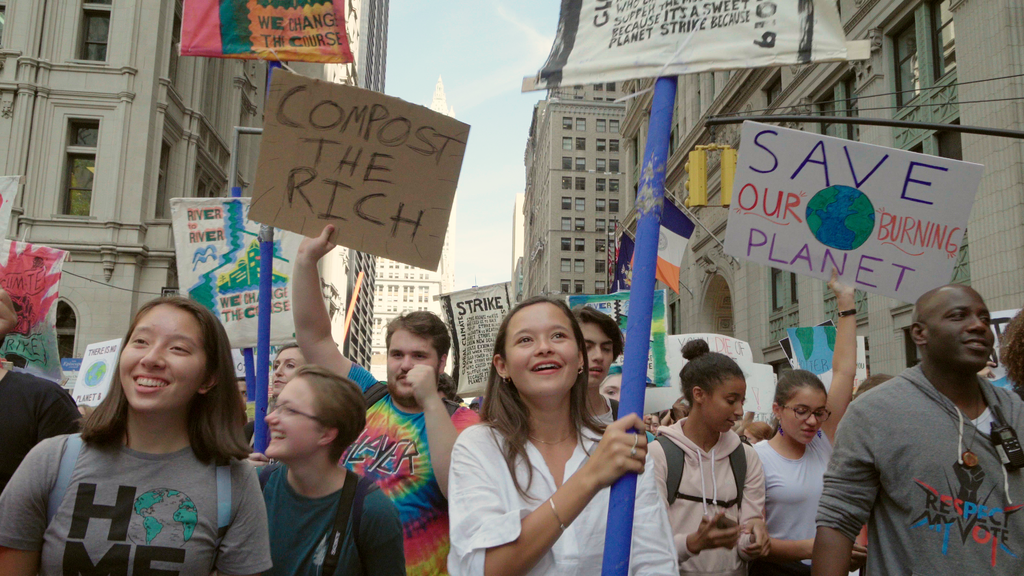 Klimaatactiviste Melati loopt mee tijdens een klimaatprotest en houd een protestbord omhoog. 