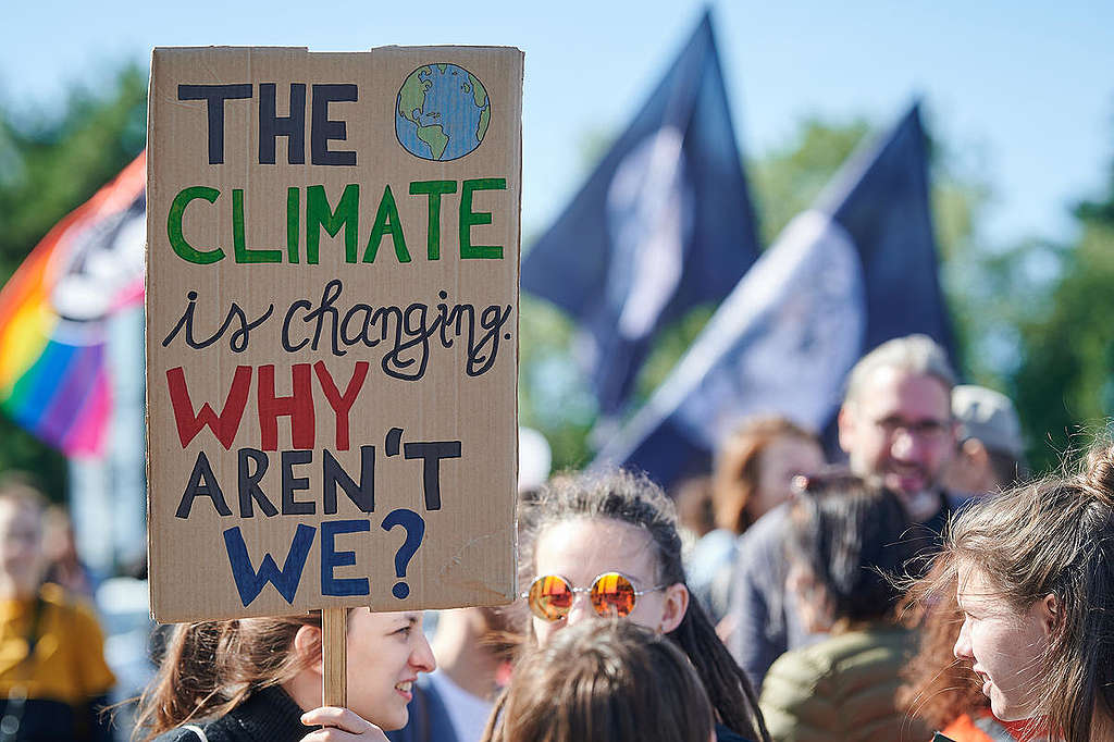 Een vrouw draagt een protestbord met de tekst: 'the climate is changing. Why aren't we?