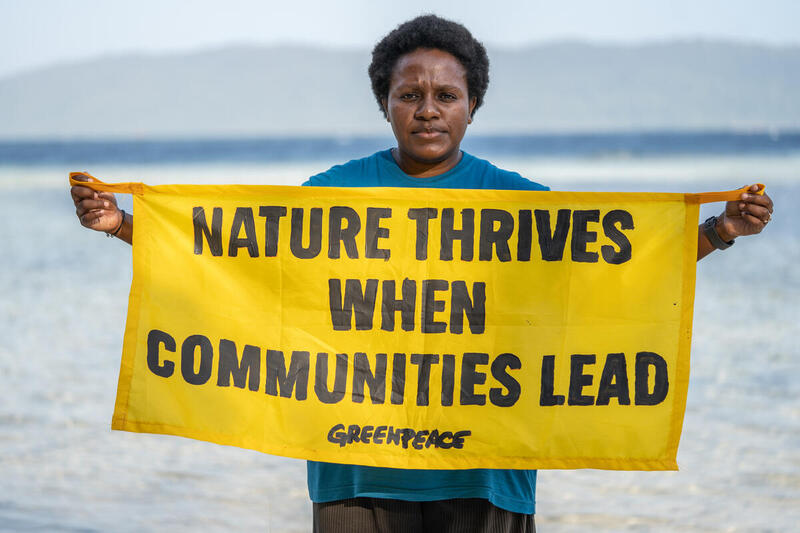 Spandoek voor Inheemse rechten bij natuurbescherming vastgehouden door een activist waarop staat: natuur floreert als gemeenschappen leiden