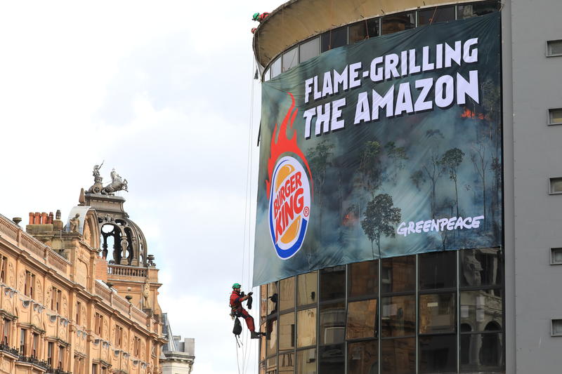 Greenpeace-klatrere rappellerer fra taket på Burger Kings ikoniske restaurant på Leicester Square i London. Et gigantisk banner knytter hurtigmatkjeden til rekordbrannene og avskogingen av regnskogen i Amazonas.