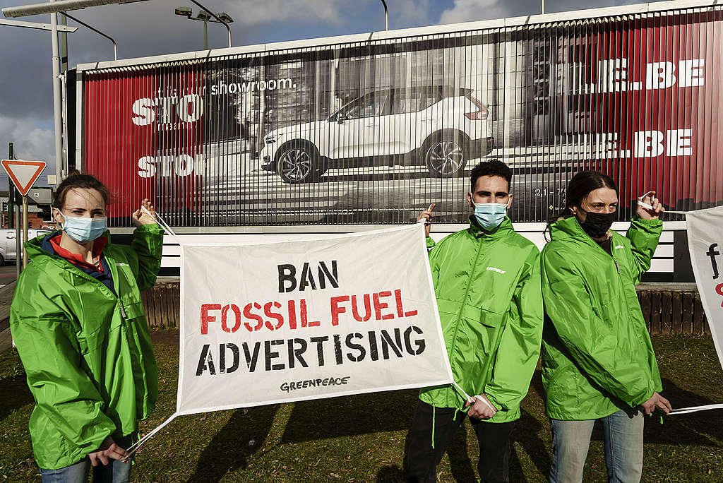 Aktivister fra Greenpeace med et banner som sier "Ban fossil fuel advertising" foran en bilannonse i Brussel i Belgia.