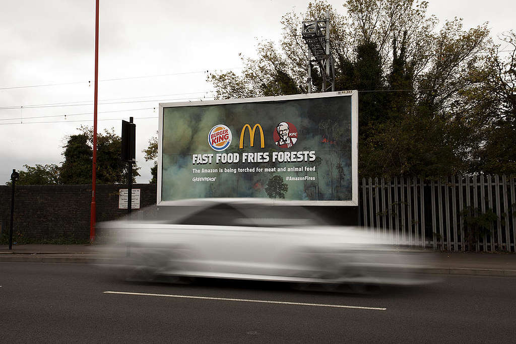 Reklametavler fremhever hurtigmatindustriens rolle i ødeleggelsen av Amazonas. På plakaten står det "Fast Food Fries Forests. The Amazon is being torched for meat and animal feed."