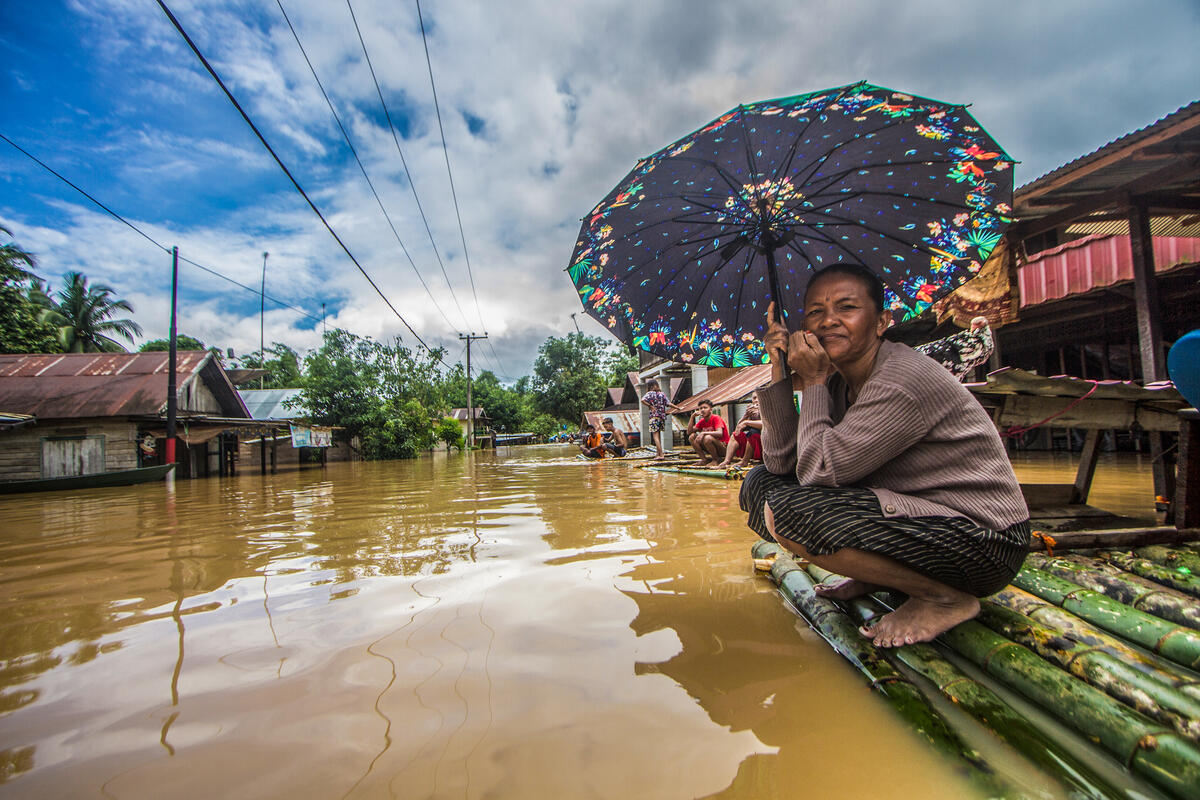 En kvinne holder en paraply mens hun venter på å bli evakuert av redningsteamet på en bambusflåte foran hennes oversvømmede hus i landsbyen Sungai Raya, Banjar Regency, Sør-Kalimantan i Indonesia. © Putra / Greenpeace