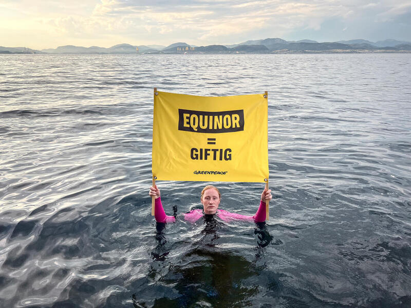 Greenpeace-aktivist Aman­da Louise Hel­le i vannet utenfor Mongstad, med banner som sier "Equinor = giftig".