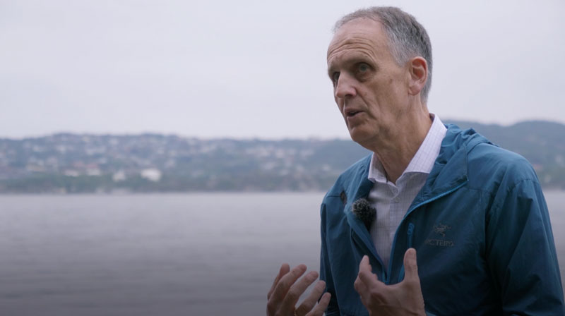 Havforsker Peter Haugan står foran et disig kystlandskap. Han har på seg blå vindjakke, hvit skjorte og gestikulerer mens han prater.