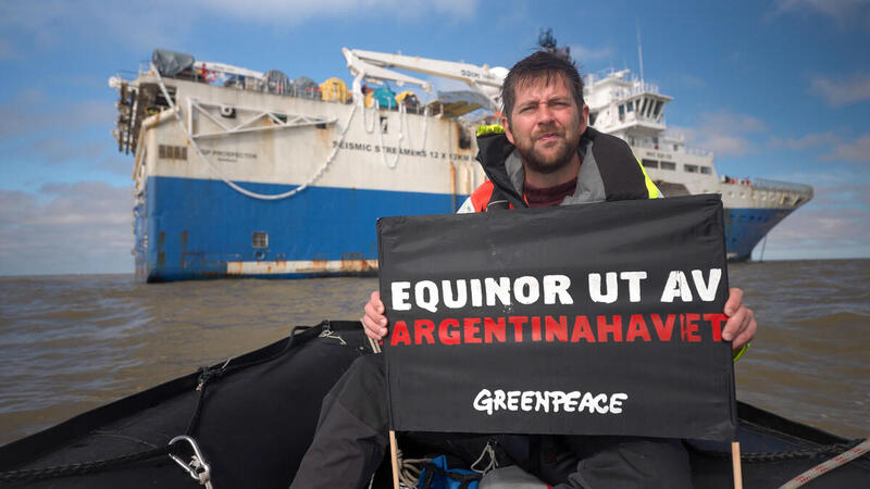 Activist Halvard Raavand holds banner with message "Equinor out of the Argentine Sea" in front of ship due to carry out seismic shooting. Aktivist Halvard Raavand holder et banner med beskjeden "Equinor ut av Argentinahavet" foran skipet som Equinor har hyret for å utføre seismikkskyting.