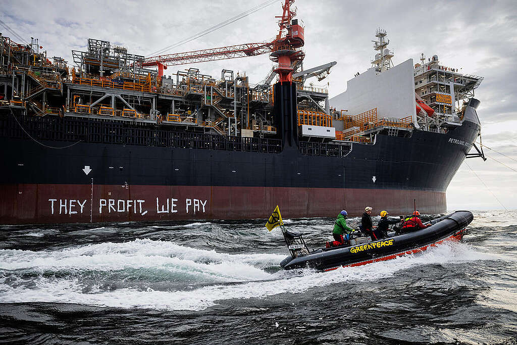 Aktivister i båt foran produksjonsskipet som Equinor vil bruke på Rosebank-feltet i Storbritannia. Aktivistene har malt "They profit, we pay" på siden av skipet.
