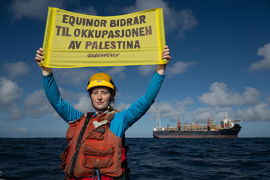 Norsk aktivist Amanda Louise Helle-Rasmussen foran et gigantisk produksjonsskip utenfor kysten av Namibia. som Equinor vil bruke på oljefeltet Rosebank. Tekst på banneret: "Equinor bidrar til okkupasjonen av Palestina"