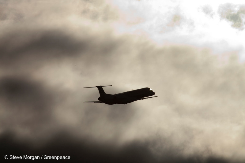 Svart flygplan, som ser ut som en silhuett, flyger bland gråa moln.