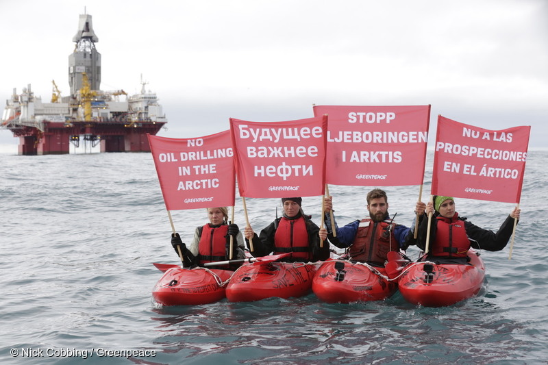 4 Greenpeace-aktivister på kajaker intill en oljerigg i Arktis som håller upp en flagga med texten "Stoppa oljeborrningen i Arktis"