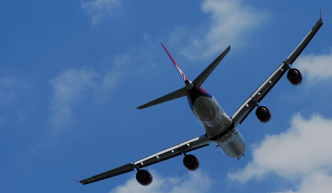 Stort passagerarflygplan i luften, fotograferat underifrån. I bakgrunden syns blå himmel och några moln.