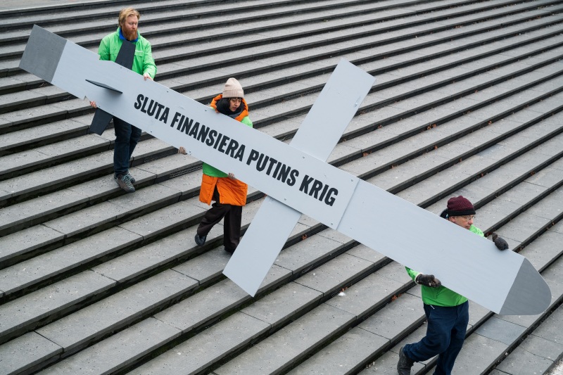 Tre Greenpeaceaktivister bär en banderoll i form av en rysk kryssningsmissil med texten "SLUTA FINANSIERA PUTINS KRIG"  
