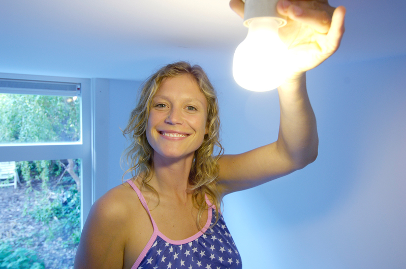 Ung kvinna skruvar i energisnål glödlampa