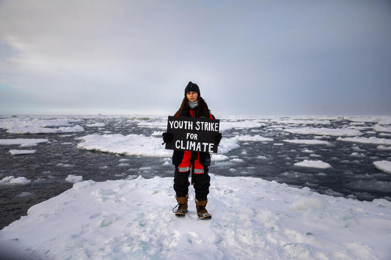 Ung aktivist på smältande isar i Arktis håller skylt med text: Youth Strike for Climate" under världens nordligaste klimatstrejk