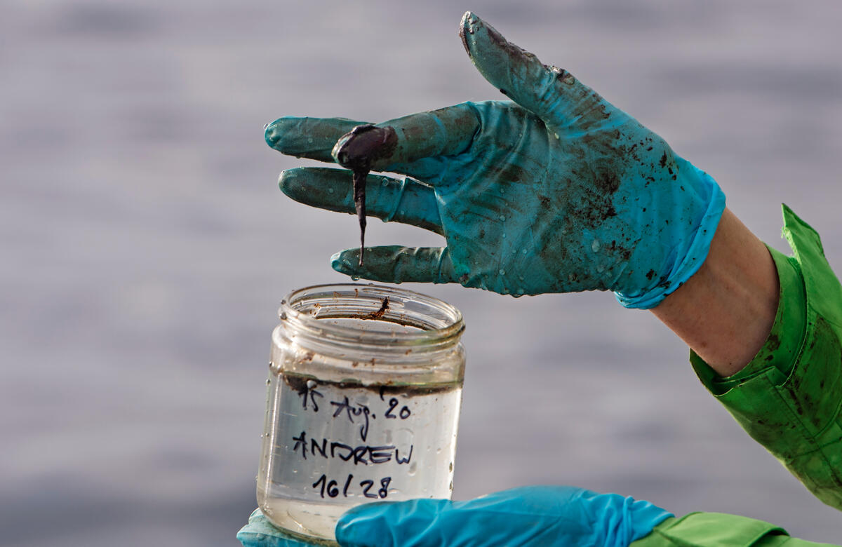 綠色和平德國辦公室海洋專案主任Sandra Schoettner帶著手套，手持北海鑽油臺附近的海水樣本，已明顯看出沾染油污。