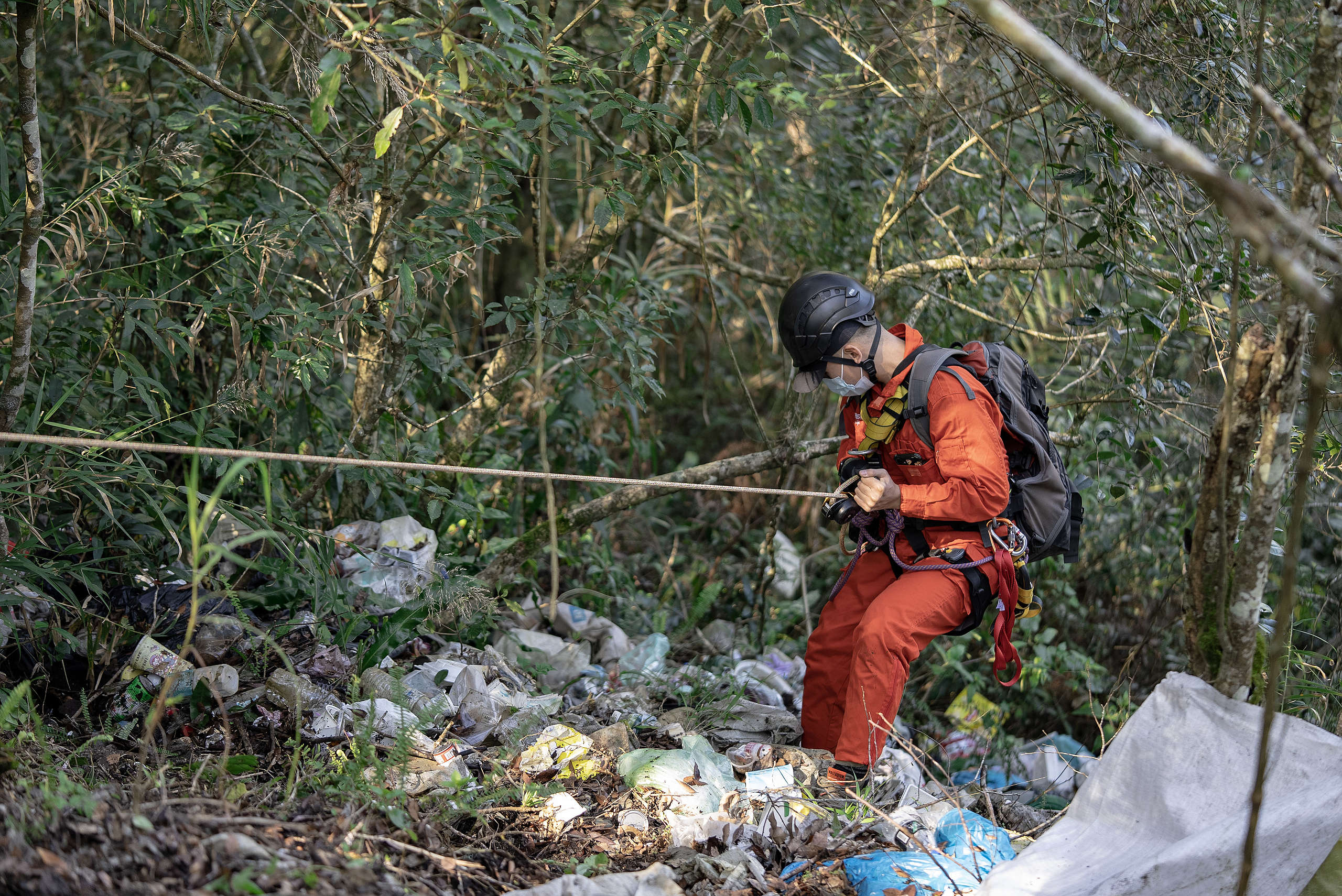 綠色和平行動者在滿是垃圾的山壁上，以繩索垂降撿拾廢棄物。