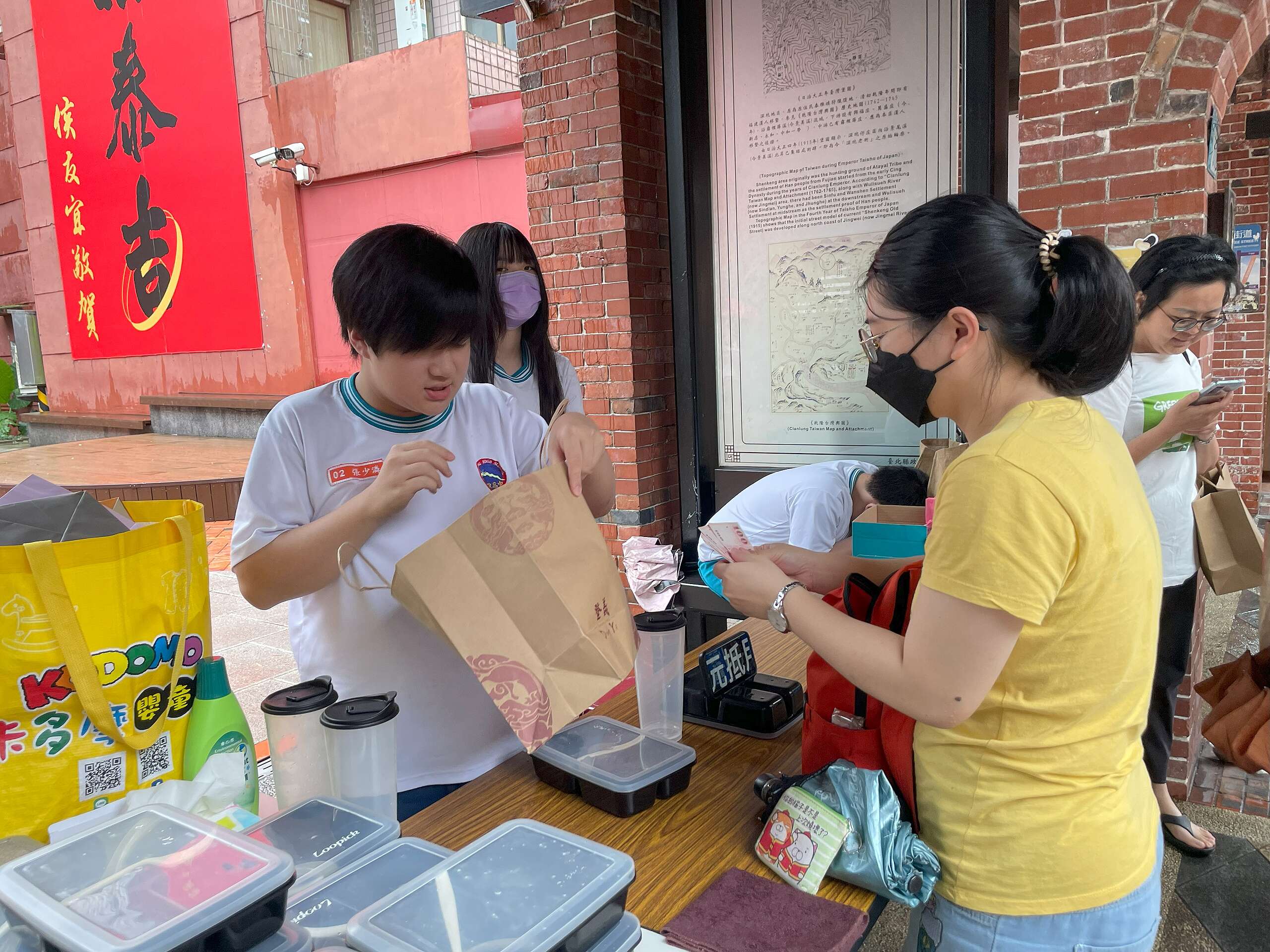 循環餐具租借站站長張少潾(左一),正向遊客耐心解說借還流程、收取押金,並將出借的餐具妥善放入紙袋,方便遊客攜帶。