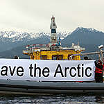A Greenpeace RHIB displays a "Save The Arctic"  banner as the Polar Pioneer, a 400-foot-tall rig owned by Transocean and leased by Royal Dutch Shell, arrives on the Blue Marlin cargo lift ship. The rig, transported from Asia, will be staged in Seattle before heading to the Arctic waters off Alaska if Shell gets permission.